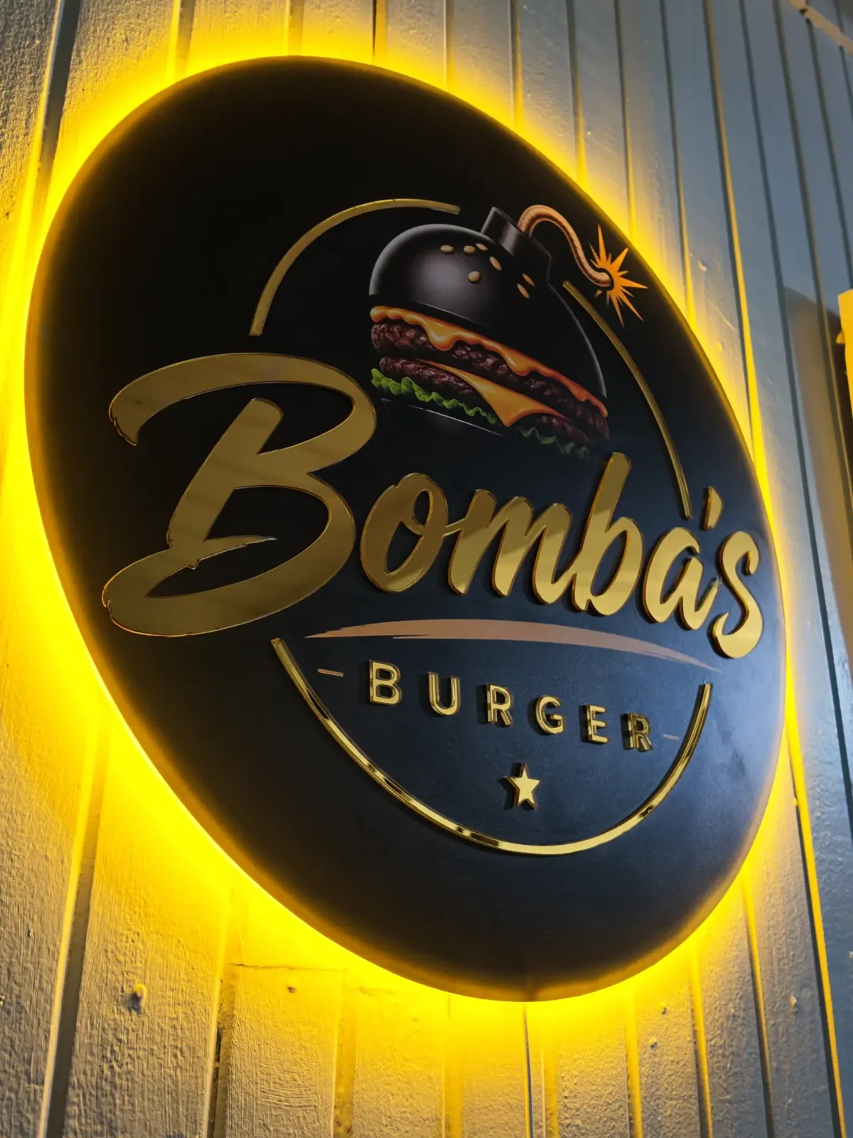 Rótulo circular retroiluminado de Bomba's Burger con letras doradas y luz LED amarilla